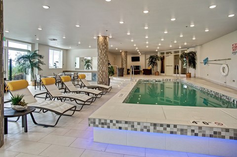 A large indoor swimming pool with lounge chairs and a tiled edge.