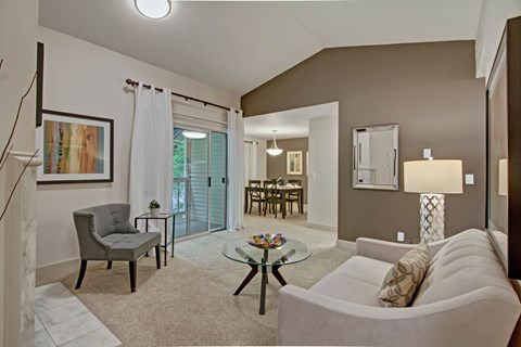 A living room with a grey couch, a glass table, and a painting on the wall.