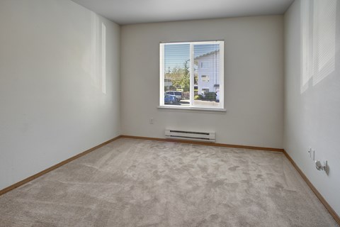 A room with a carpeted floor and a window showing a view of a house and trees.