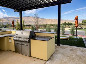 an outdoor kitchen with a grill and a table with umbrellas in the background