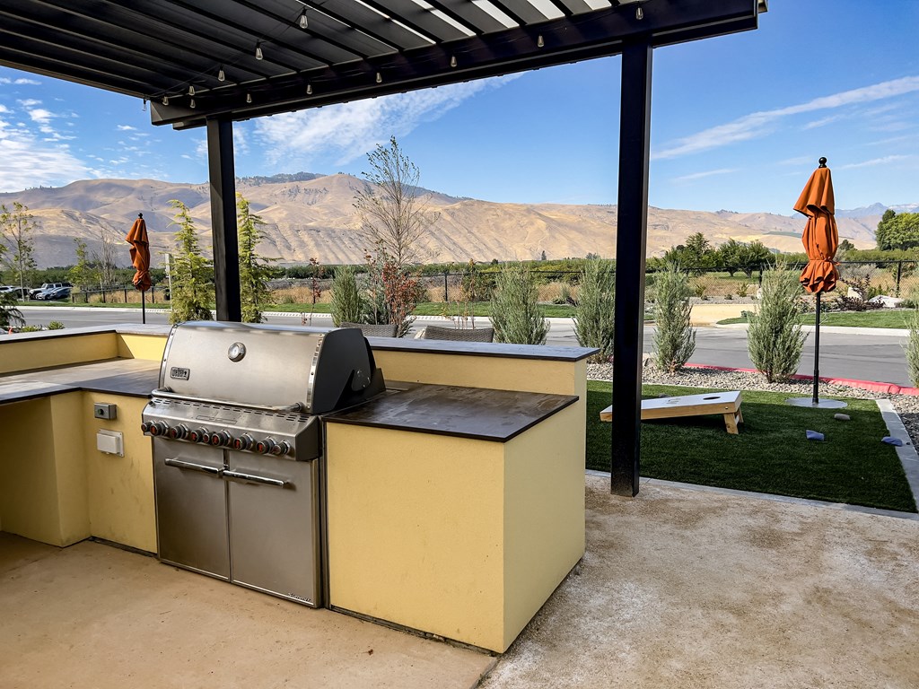 an outdoor kitchen with a grill and a table with umbrellas in the background