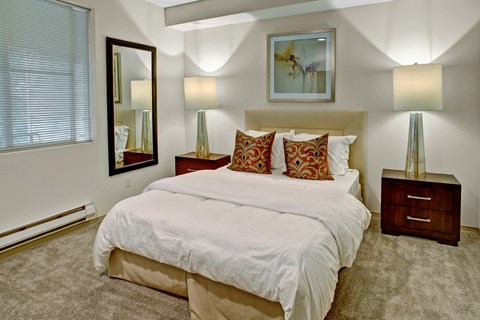 A bedroom with a large bed, two lamps, and a painting on the wall.