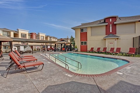 A pool surrounded by red chairs and a building in the background.
