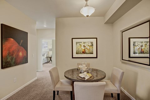 A dining room with a table set for two and a painting on the wall.