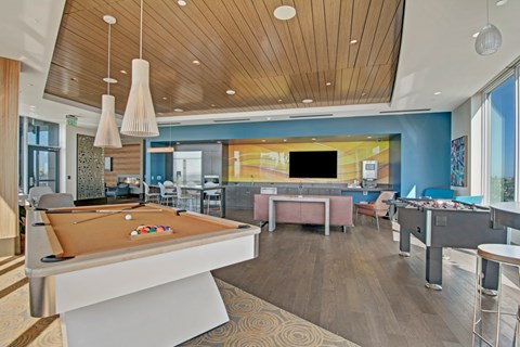 A billiard table is in the middle of a room with a bar and a television.