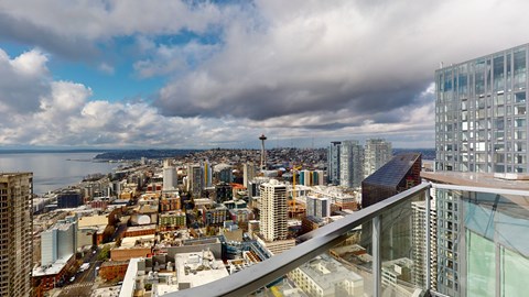 A cityscape with a mix of modern and older buildings, a cloudy sky, and a body of water in the distance.