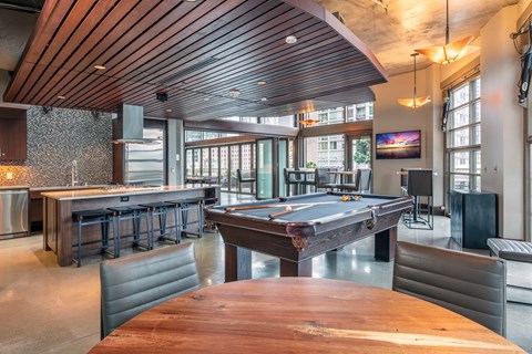 A pool table is in the middle of a room with a bar and a television.