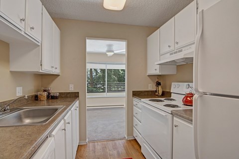 A kitchen with white cabinets and appliances, a window, and a view of trees outside.