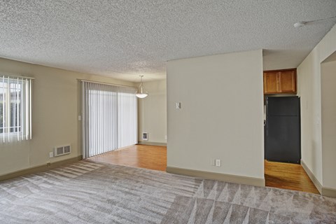 A spacious living room with a grey carpet and a black refrigerator in the corner.