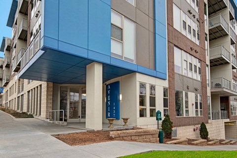 A welcoming exterior entrance here at Avenir featuring modern blue architectural accents, clean lines, and large windows. The contemporary design and landscaped surroundings create a polished, inviting first impression.