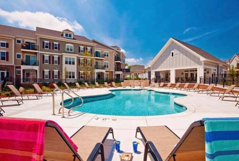A large swimming pool surrounded by lounge chairs and umbrellas in front of a building.