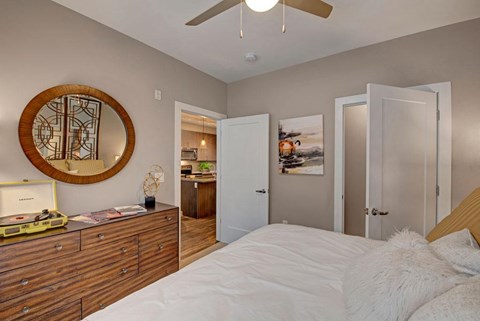 A cozy bedroom here at River House featuring a white bed with warm gold pillows, a large wooden dresser sits across the bed with a rounded mirror, and a ceiling fan light brightening the space.