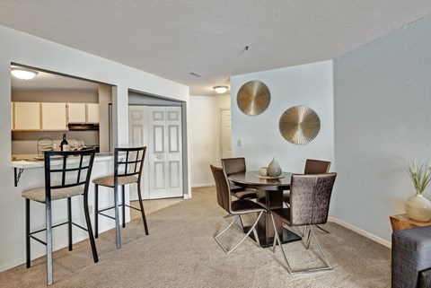 A cozy dining area here at River’s Cove with a round table, brown upholstered chairs, and gold wall accents. The breakfast bar with black stools adds a welcoming space for casual dining and entertaining.