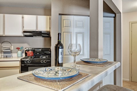 A bright kitchen here at River’s Cove featuring a breakfast bar with decorative blue plates, wine glass, and bottle. Light cabinetry and an open pass-through create a clean, inviting space perfect for casual dining.