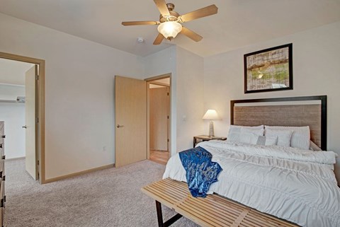 A cozy bedroom here at Swan Creek with plush carpet, warm wood trim, ceiling fan, and bright lighting, creating a comfortable, inviting, and relaxing space with convenient closet access.
