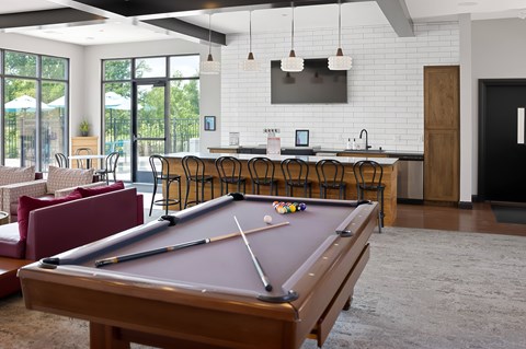 A pool table is in the middle of a room with a bar and a television.