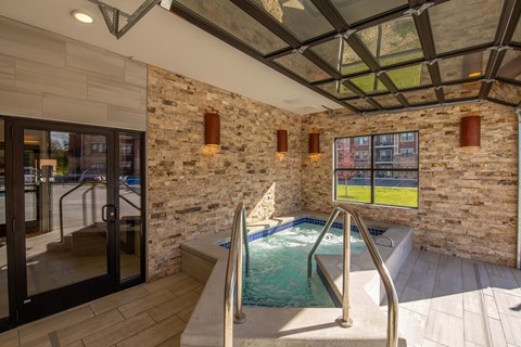 A relaxing spa room here at The Park featuring a bubbling hot tub, stone accent walls, large windows, glass garage-style door, and warm lighting, creating a luxurious and tranquil retreat space.