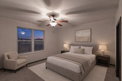 A calm bedroom here at The Park with soft neutral bedding, matching nightstands with lamps, a cozy accent chair, and plush carpet, creating a peaceful, spacious, and inviting retreat.
