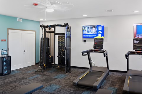 A gym with treadmilers, a weight machine, and a television.