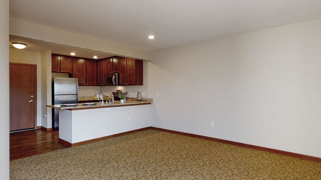 an empty living room with a kitchen in the background