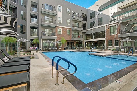 Our modern Park on Central Apartment complex courtyard with a sparkling pool, lounge chairs, and striped umbrellas. Overlooking balconies enhance the calm, inviting atmosphere.