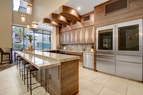 Elegant modern resident lounge kitchen here at Park on Central Apartments with large island, bar stools, and textured cabinets. Features pendant lights, stainless steel appliances, and large windows.