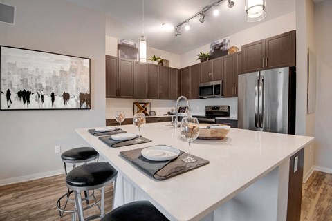 Modern kitchen here at Park on Central Apartments with dark cabinets, stainless steel appliances, and a white island. Three stools and set places suggest a welcoming, elegant atmosphere.