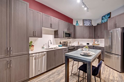 Modern kitchen here at Park on Central Apartments with gray cabinets, stainless steel appliances, and a wooden island. Warm lighting and decorative wall art create a cozy ambiance.