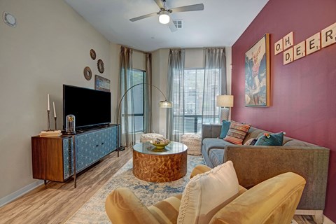 Cozy living room here at Park on Central Apartments with a maroon accent wall, modern decor, and playful tones. Features a gray sofa, patterned cushions, round coffee table, and TV.