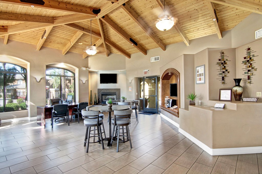 Spacious lobby here at Reserve at Arrowhead Apartments with wooden ceiling beams, tiled floor, and soft lighting. Features a fireplace, modern furniture, and large windows with garden views.