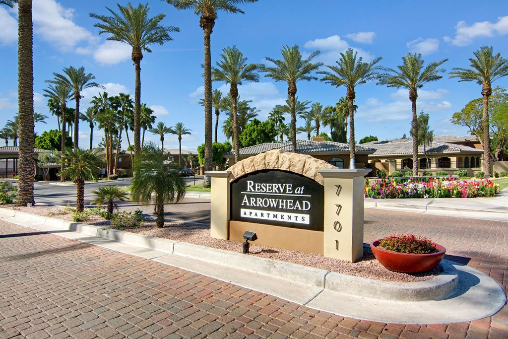 Entrance to Reserve at Arrowhead Apartments features a stone sign amid palm trees and manicured landscaping, exuding a welcoming, resort-like ambiance.