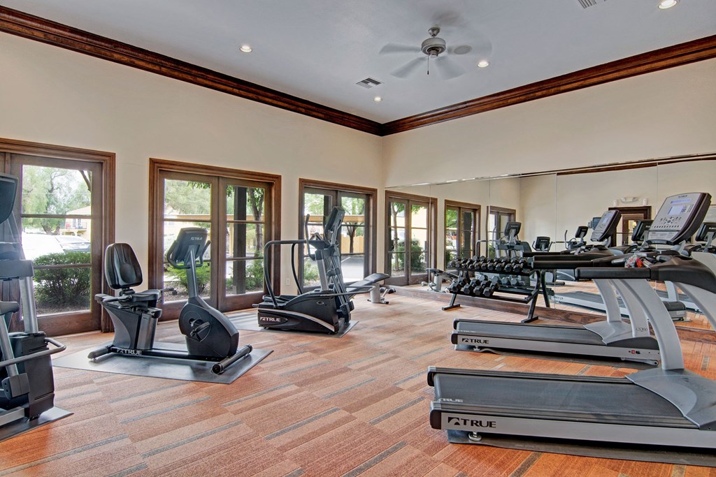 Bright gym here at The Retreat at Speedway Apartments with treadmills, stationary bikes, and weights. Large windows provide natural light, reflecting a clean and inviting exercise space.