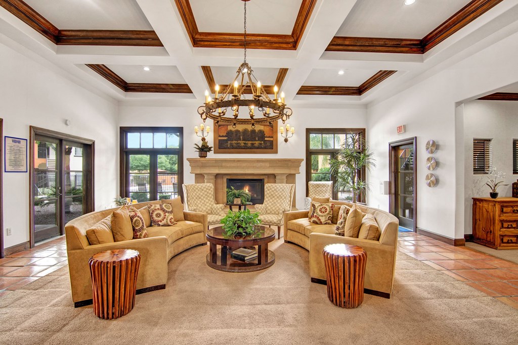 Spacious living room here at The Retreat at Speedway Apartments with cream sofas and patterned cushions around a circular table with a plant. Elegant chandelier, warm lighting, cozy atmosphere.