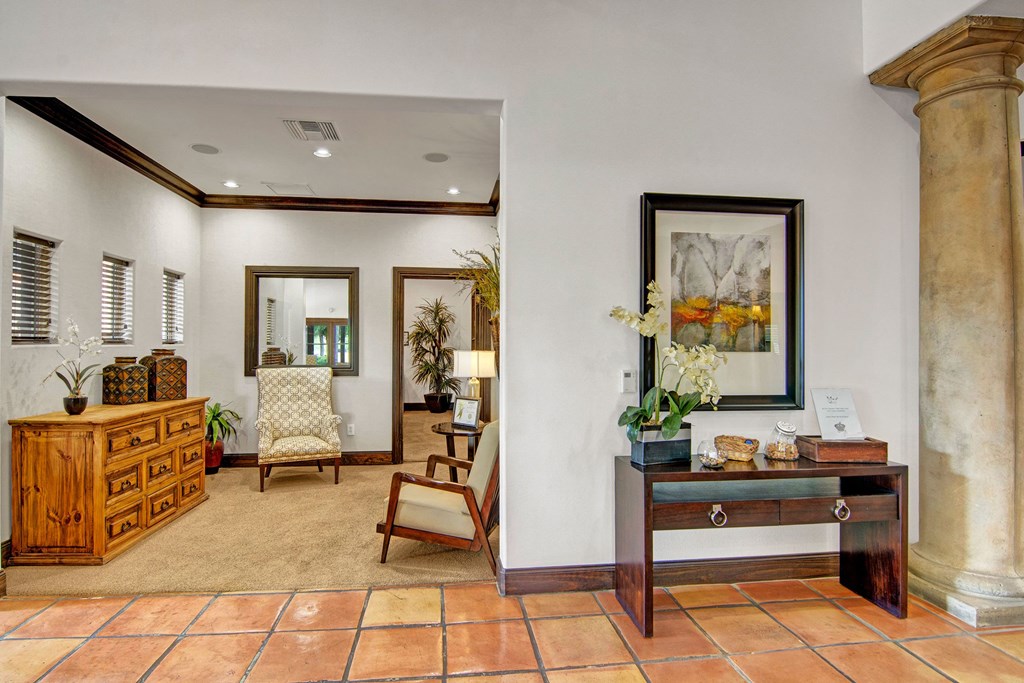 Warm, inviting office lobby here at The Retreat at Speedway Apartments with terracotta tile floors. Features elegant wooden furniture, floral decor, framed artwork, and soft, neutral tones.