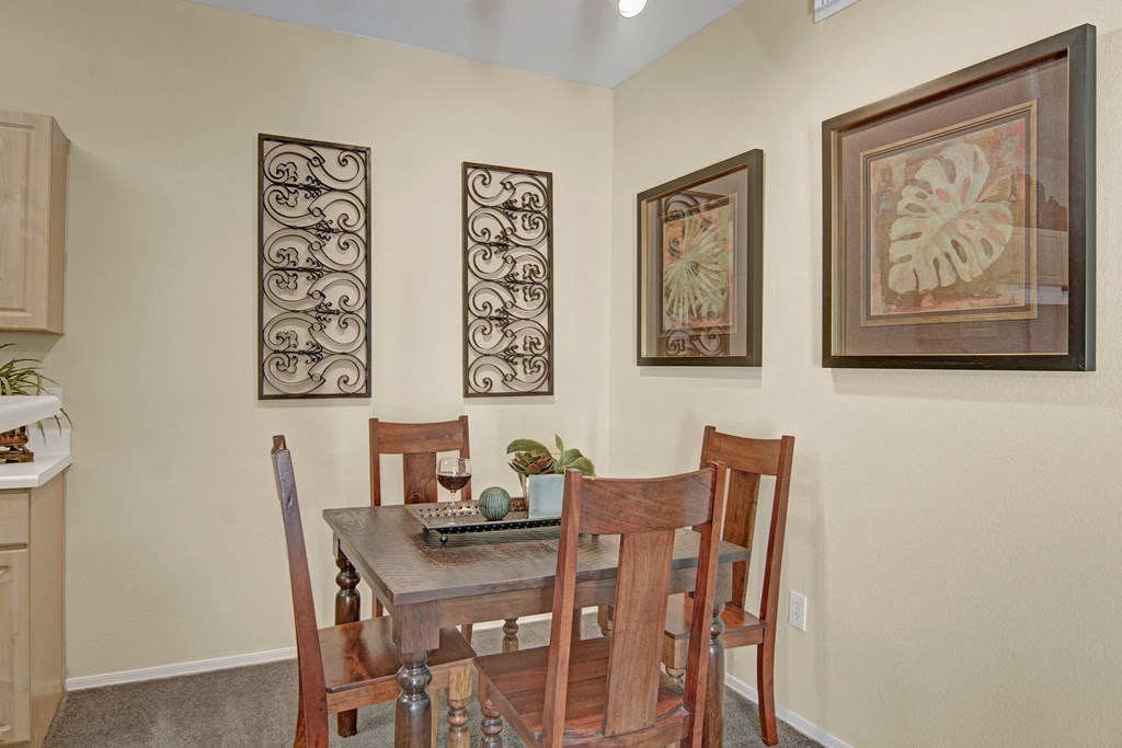 Cozy dining area here at Retreat at Speedway Apartments with a wooden table and four chairs. Walls feature decorative ironwork and leaf art. Warm lighting creates an inviting, relaxed ambiance.