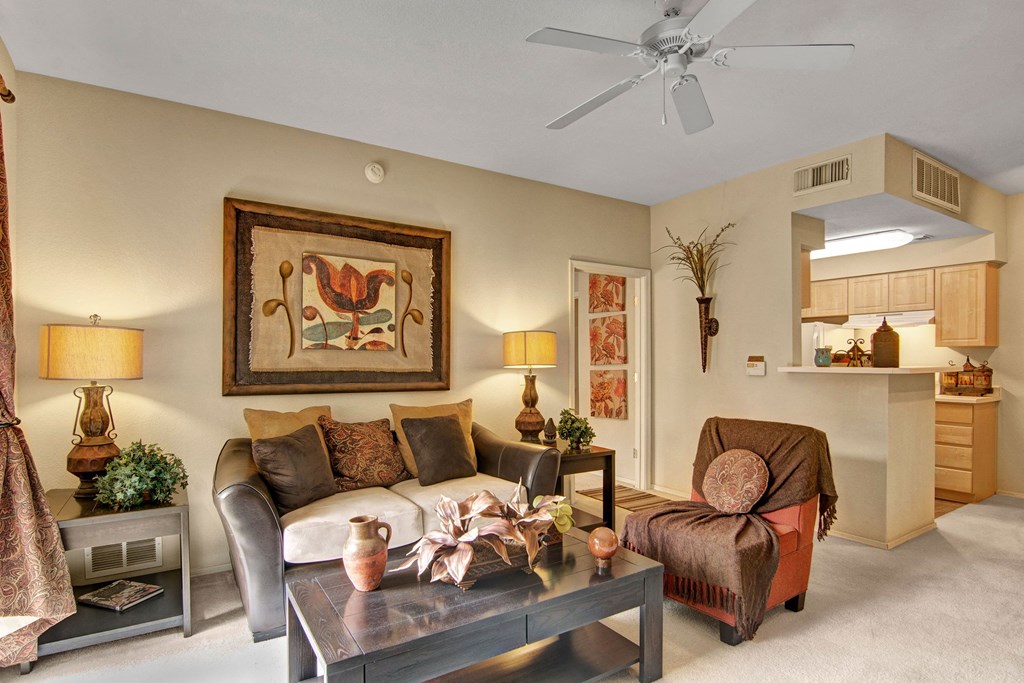 Cozy living room here at The Retreat at Speedway Apartments with a beige sofa and patterned cushions, flanked by two lamps. A large framed abstract art piece hangs above. Warm tones create a welcoming feel.