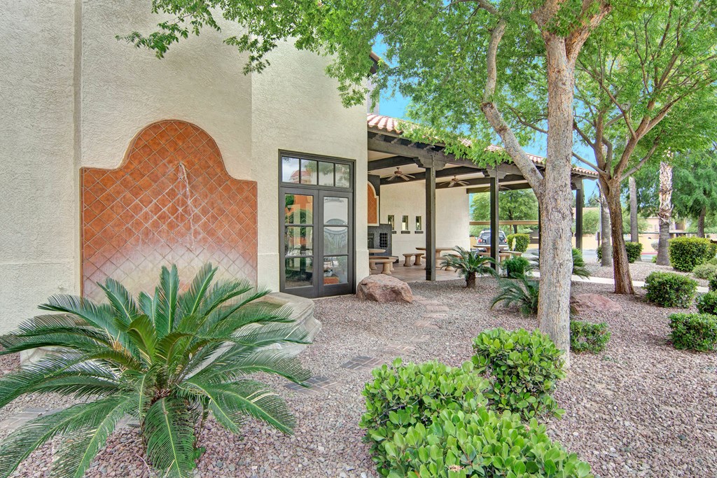 Exterior courtyard here at The Retreat at Speedway Apartments with a trellis-covered patio, stone benches, and a decorative tiled wall. Lush greenery, including trees and shrubs, create a serene atmosphere.