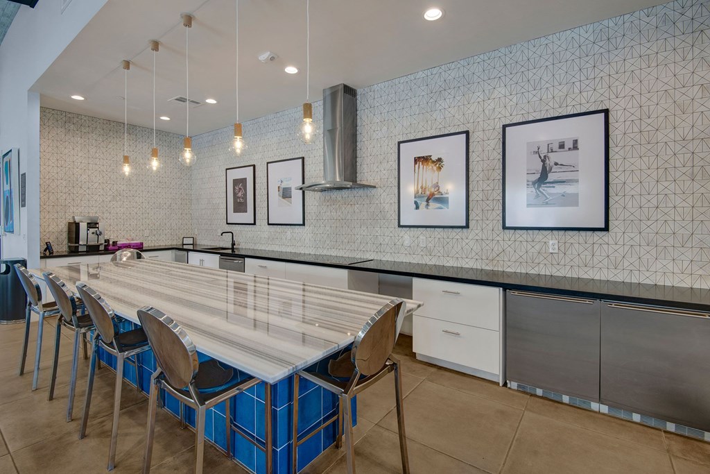 Modern kitchen here at Roosevelt Row Apartments with sleek design, featuring a marble island, metallic chairs, pendant lights, and framed art on a patterned wall. A clean, elegant ambiance.