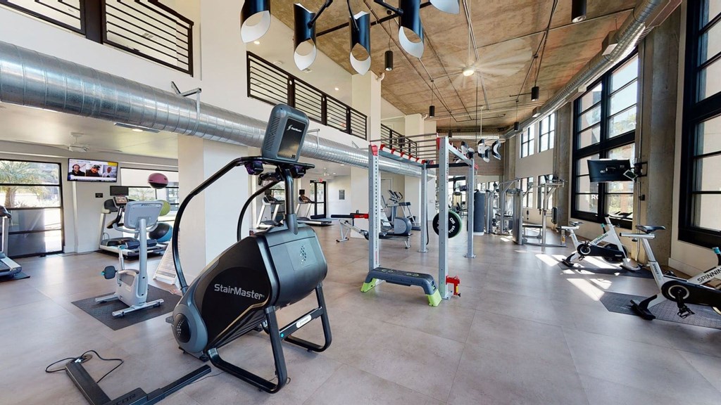 Roosevelt Row Fitness Center Spacious modern gym here at Roosevelt Row Apartments with large windows and natural light. It features a StairMaster, exercise bikes, treadmills, free weights, and sleek ductwork.