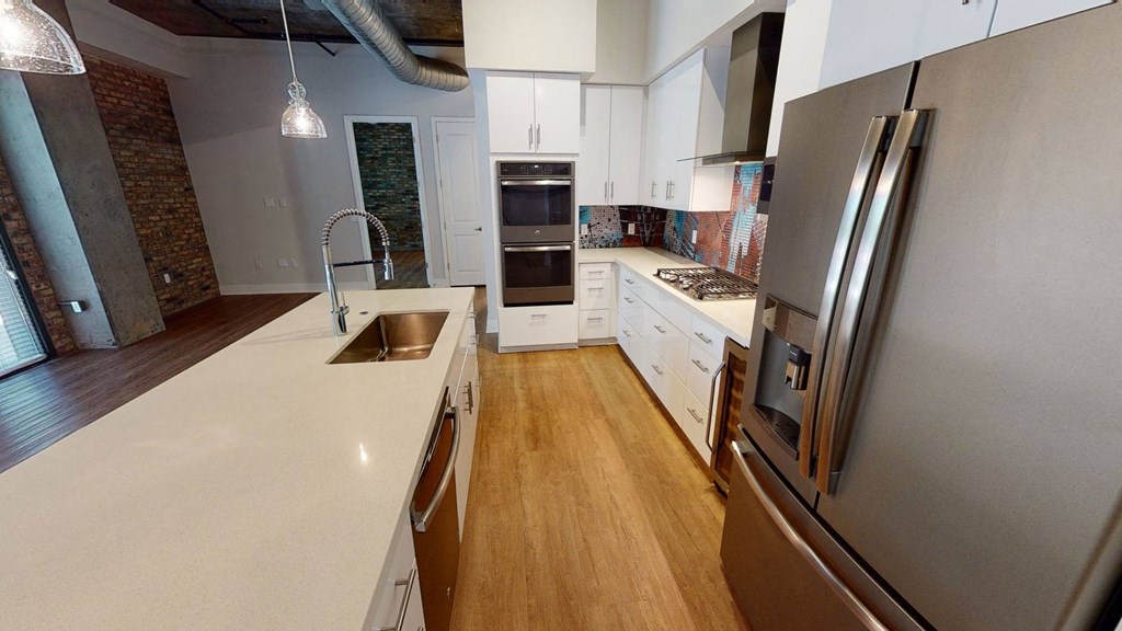 Modern kitchen here at Roosevelt Row Apartments with light wood flooring, sleek stainless steel fridge, white cabinetry, mosaic backsplash, dual ovens, and central island sink.