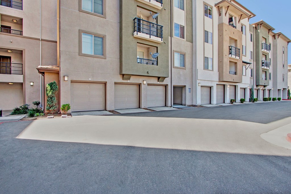 Modern Artisan at Main Street Metro Apartment complex with beige and olive exteriors. Features multiple balconies, closed garages, and small plants, creating an urban, tidy atmosphere.