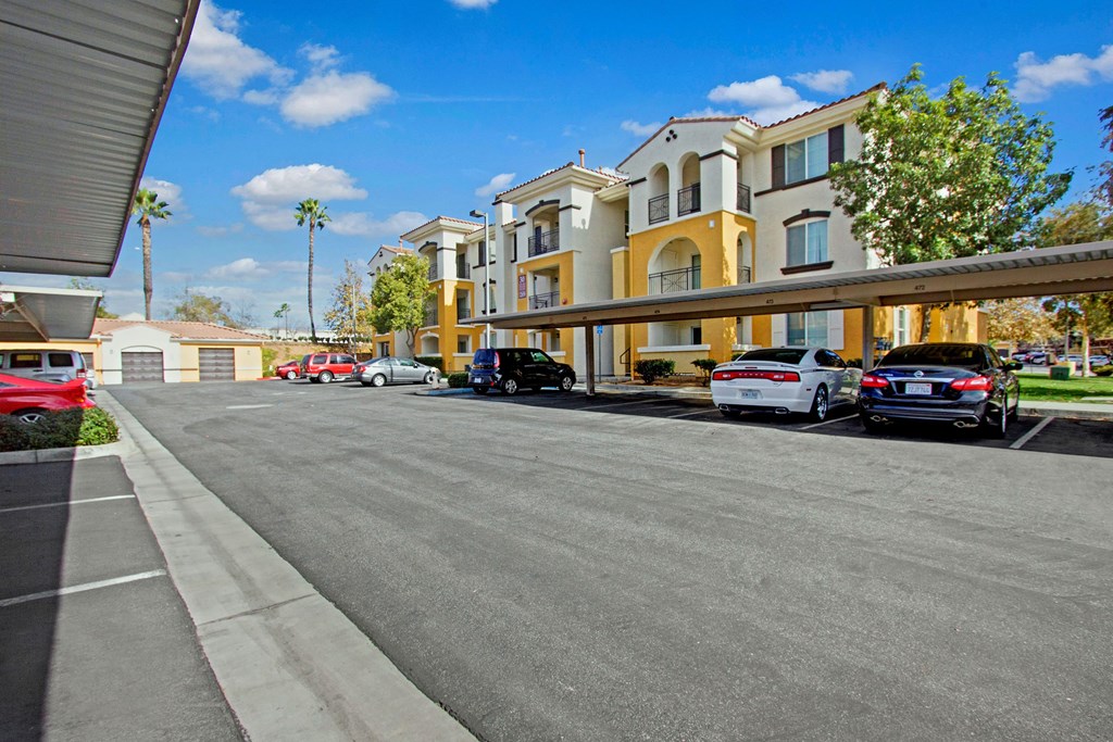 Fresco Apartment Homes complex with cream and yellow accents, surrounded by palm trees under a blue sky. Cars parked under shaded carports add a suburban, serene feel.