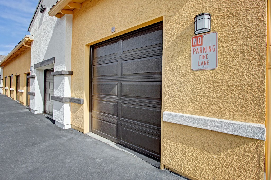 A row of textured buildings here at Fresco Apartment Homes with garage doors. A "No Parking Fire Lane" sign is mounted on a yellow wall, creating an orderly and cautionary tone.