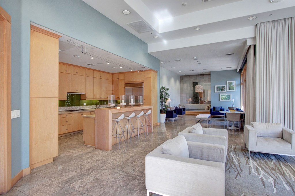 Spacious modern interior here at Vesada Apartment Homes with an open kitchen and living area. Light wood cabinets, a bar with white stools, and cozy seating areas create a welcoming atmosphere.