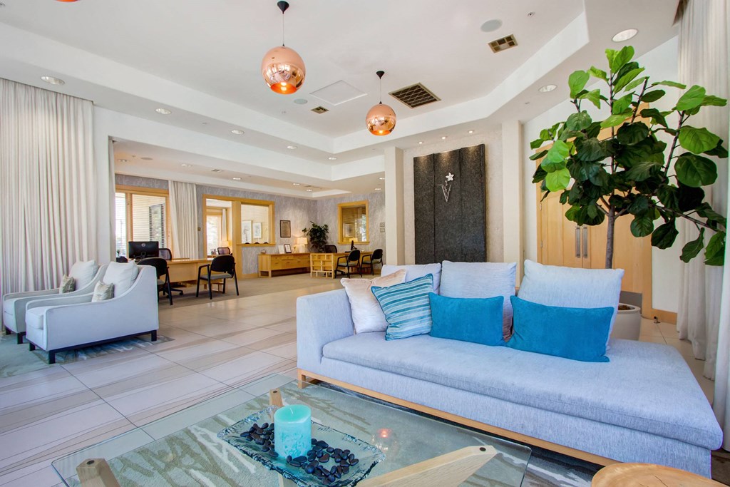 Modern living room here at Vesada Apartment Homes with light blue and white sofas, accented by blue cushions. Copper pendant lights hang above. A potted plant adds greenery.