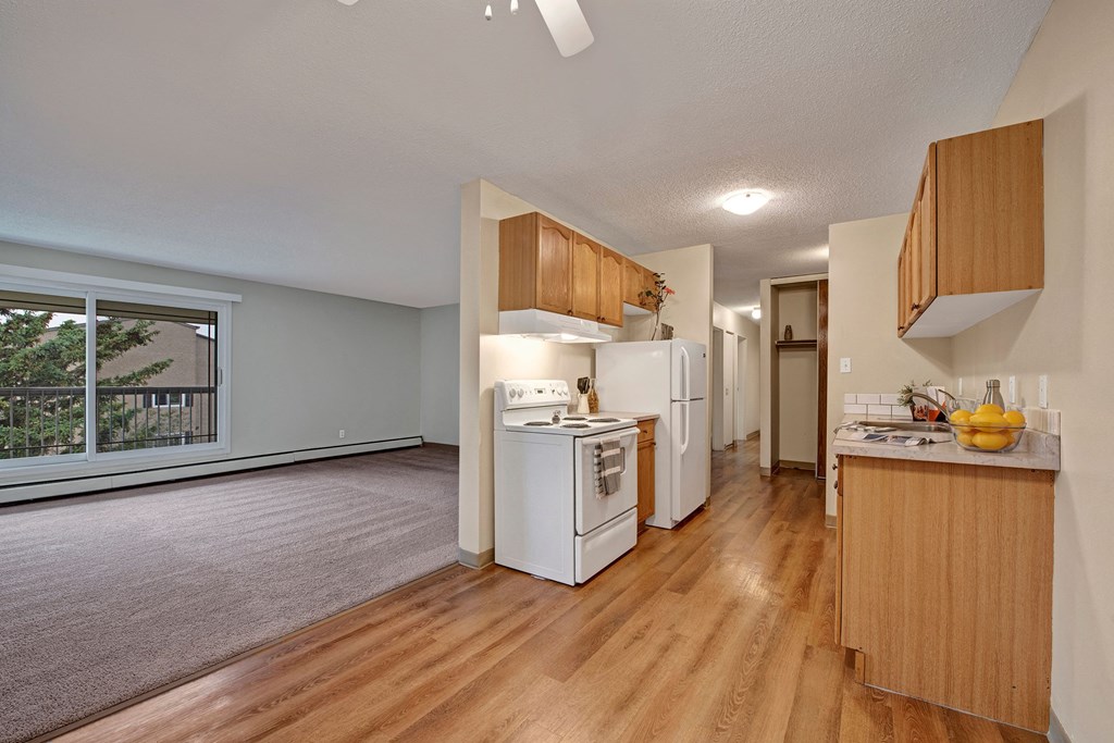 Spacious apartment interior here at Cambridge West Apartment Homes with open-plan kitchen and living area. Kitchen features wooden cabinets, white appliances, and a fruit bowl on the counter.