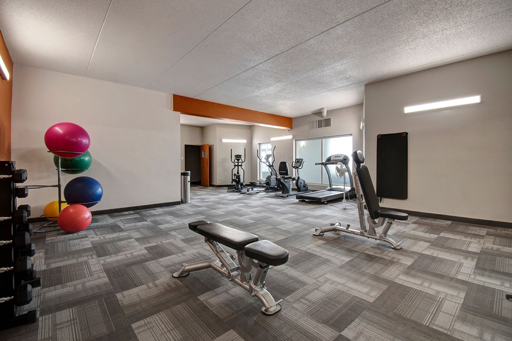 Modern gym here at Centre Pointe Plaza Apartment Homes with multi-colored exercise balls, weights, benches, and cardio machines. Bright lighting and clean, spacious layout convey a welcoming tone.