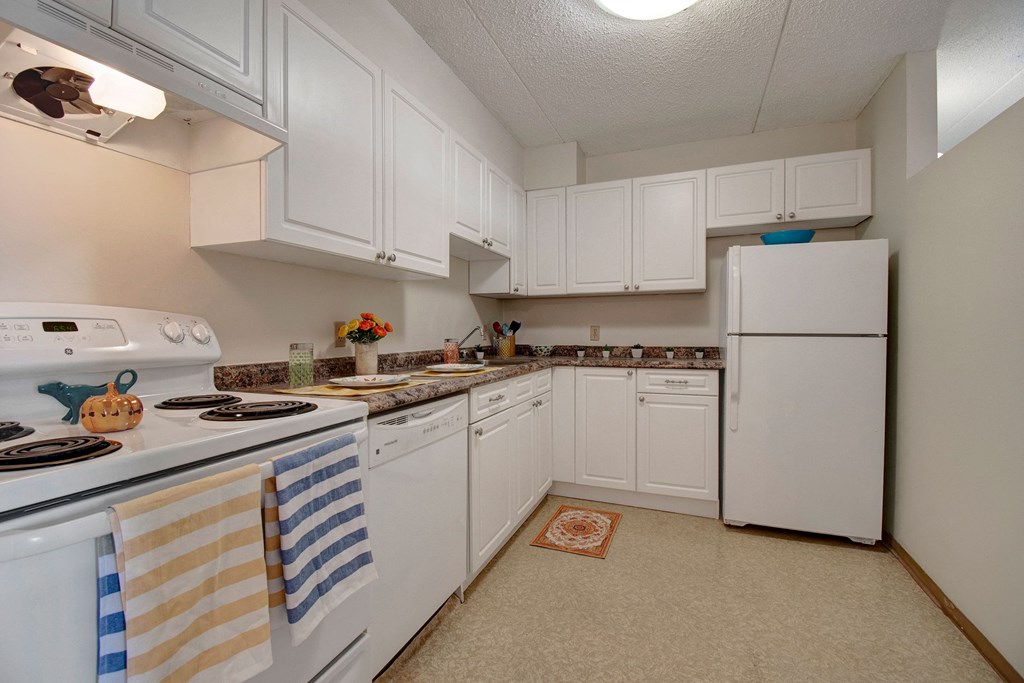 Compact kitchen here at Centre Pointe Plaza Apartment Homes with white cabinets, a countertop with decor, and appliances. Light and orderly with a pumpkin decoration adding warmth.
