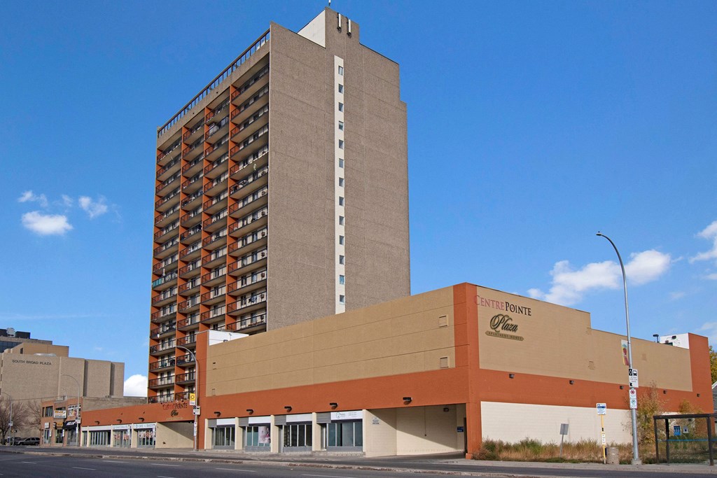 Tall, beige high-rise with red balconies centered against a clear blue sky. Foreground shows a low-rise building labeled "Centre Pointe Plaza."