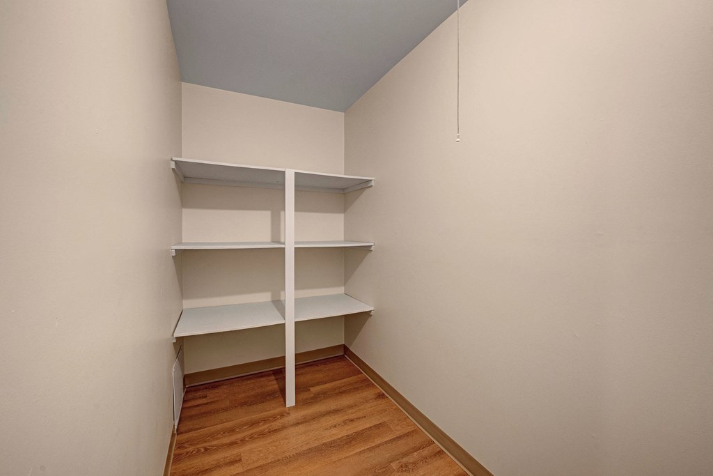 Compact storage area here at Gateway Gardens Apartment Homes with three white shelves on cream walls. Wooden floor adds warmth. Neat and functional, with a calm, minimalistic feel.